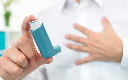 A man holds up an asthma inhaler in one hand and holds his other hand over his chest.
